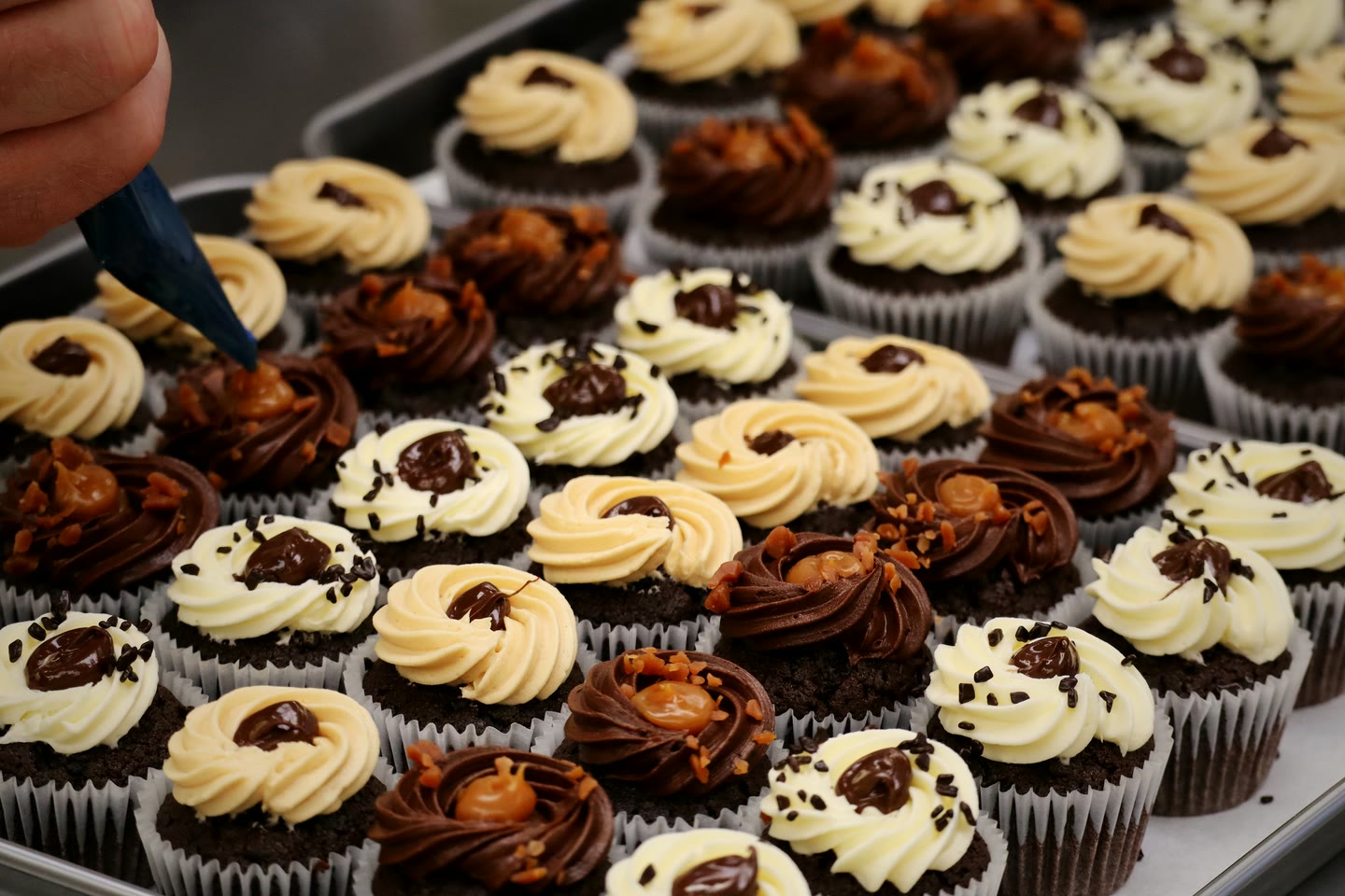 A baker hand-piping caramel buttercream onto chocolate cupcakes