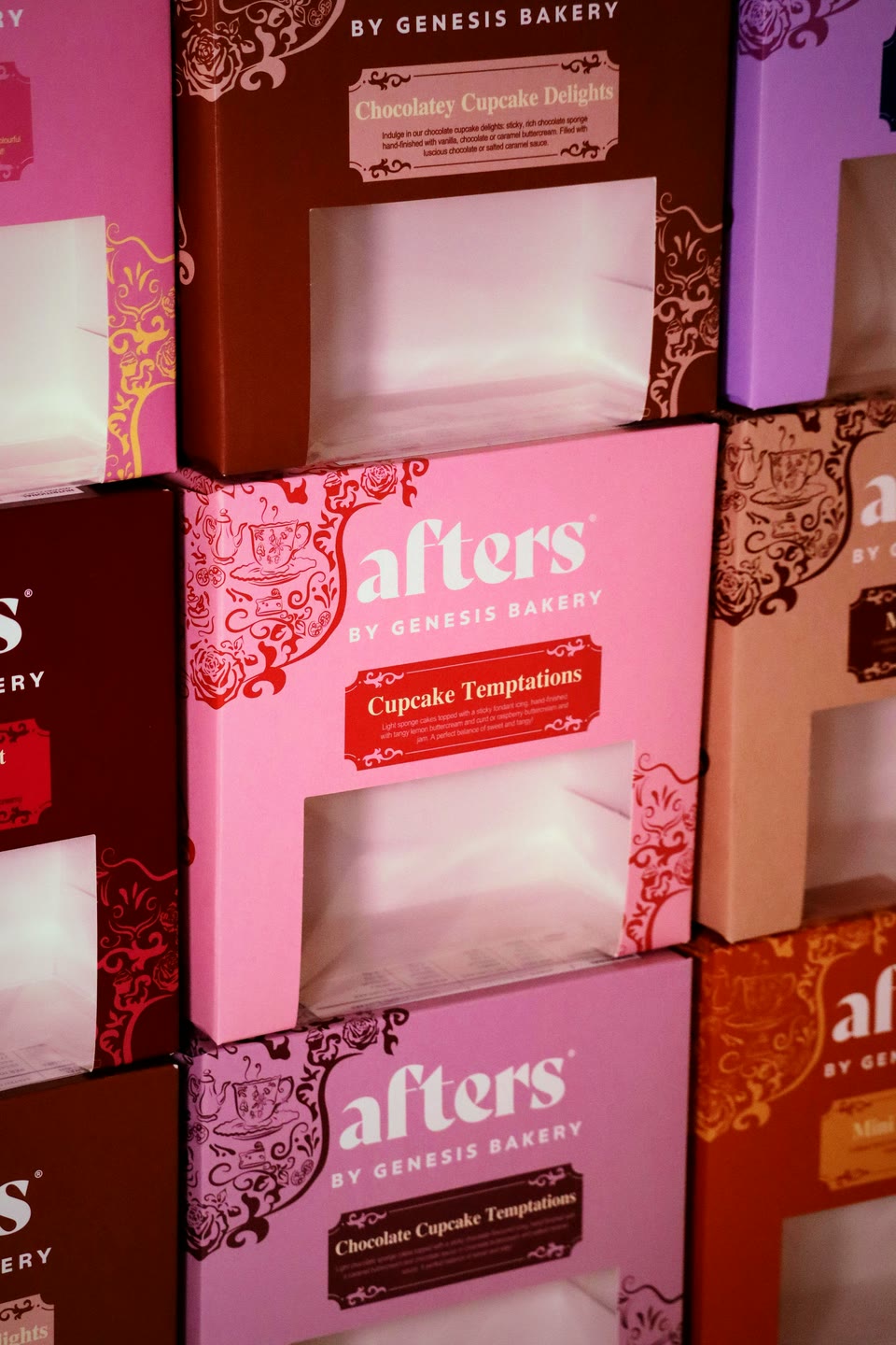 A wall of stacked afters by Genesis Bakery boxes in pink, chocolate and copper