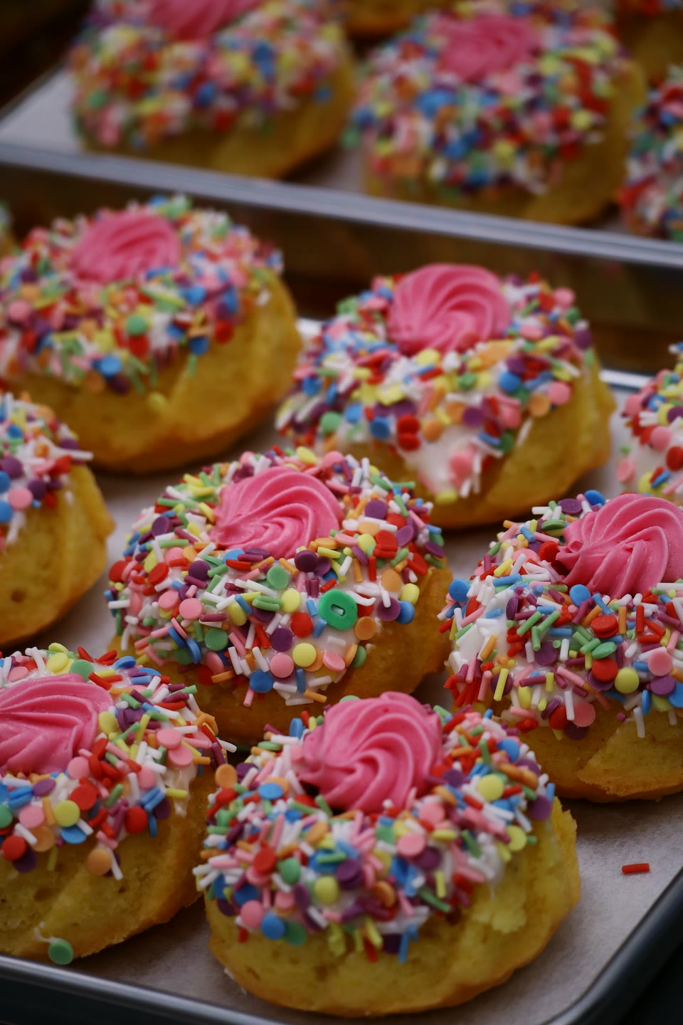 Sponge rings with pink buttercream and rainbow sprinkles on a baking tray