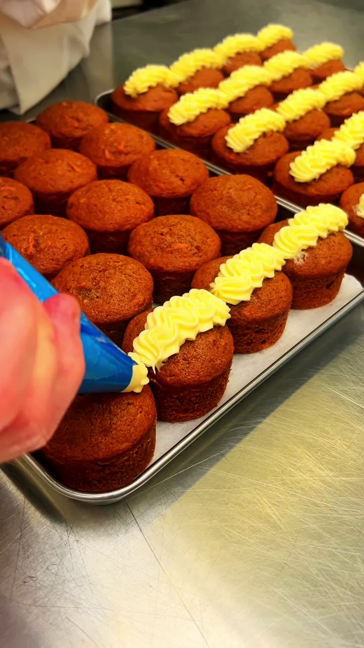A baker piping ribbons of cream cheese frosting along rows of spiced sponges