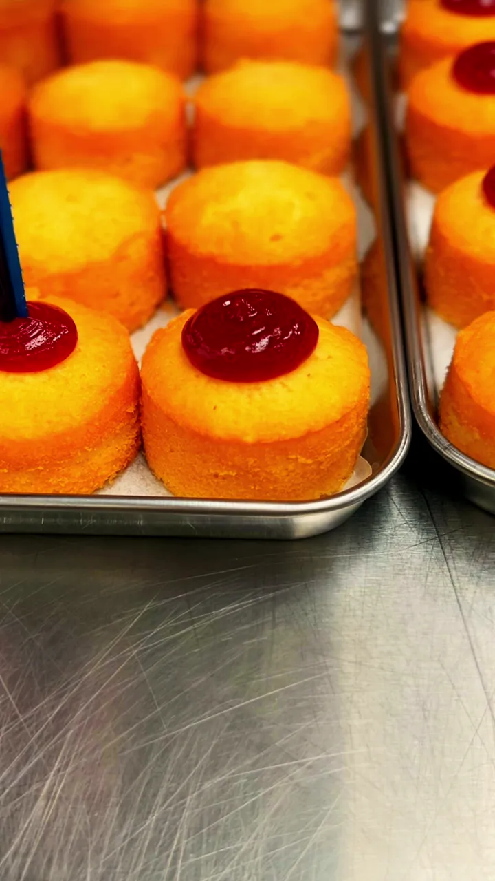Hands piping raspberry jam into rows of mini sponges