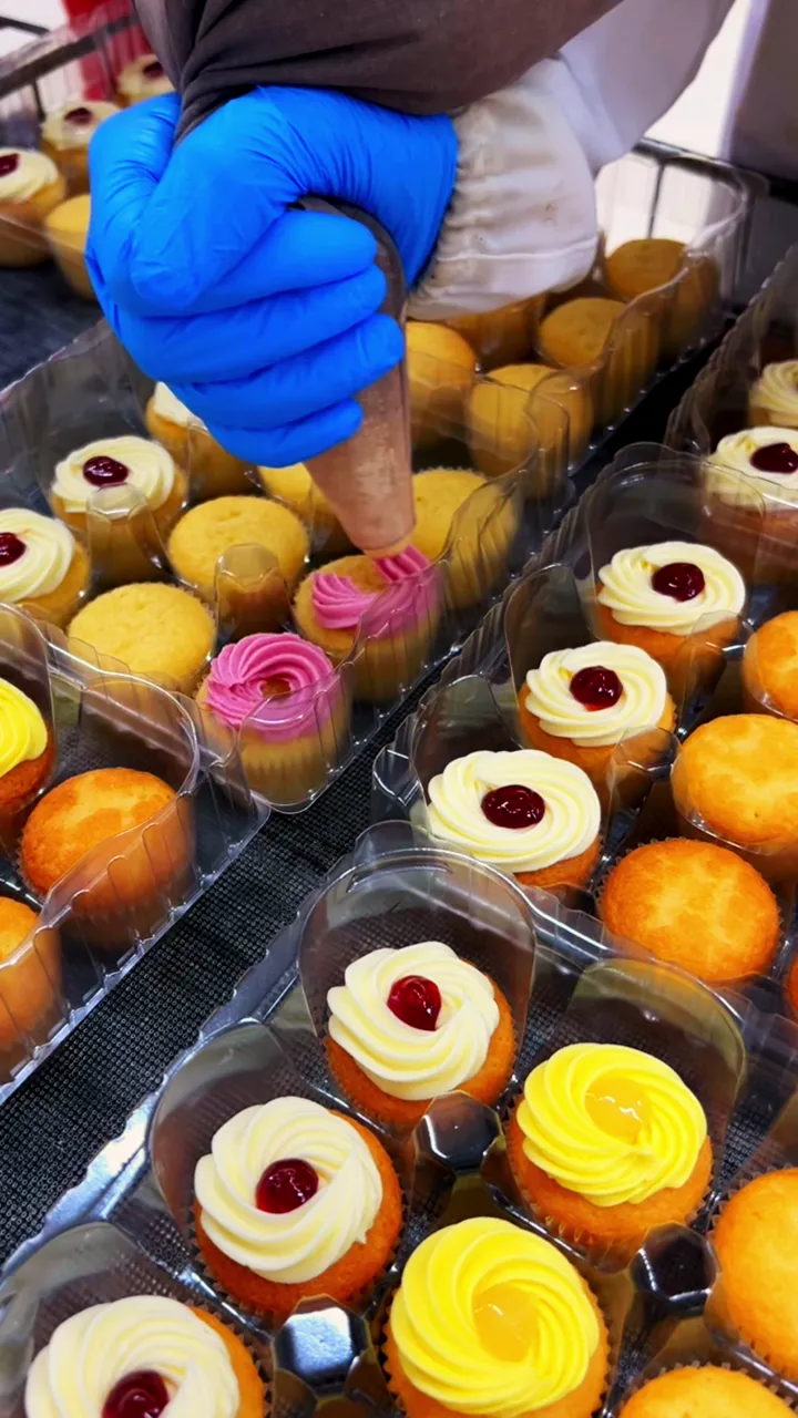 Gloved hands placing finished cupcakes into clear retail trays